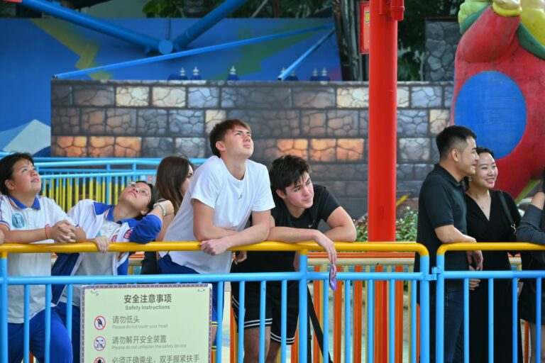 Bezoekers wachten achter hekken in de rij bij een attractie in een pretpark